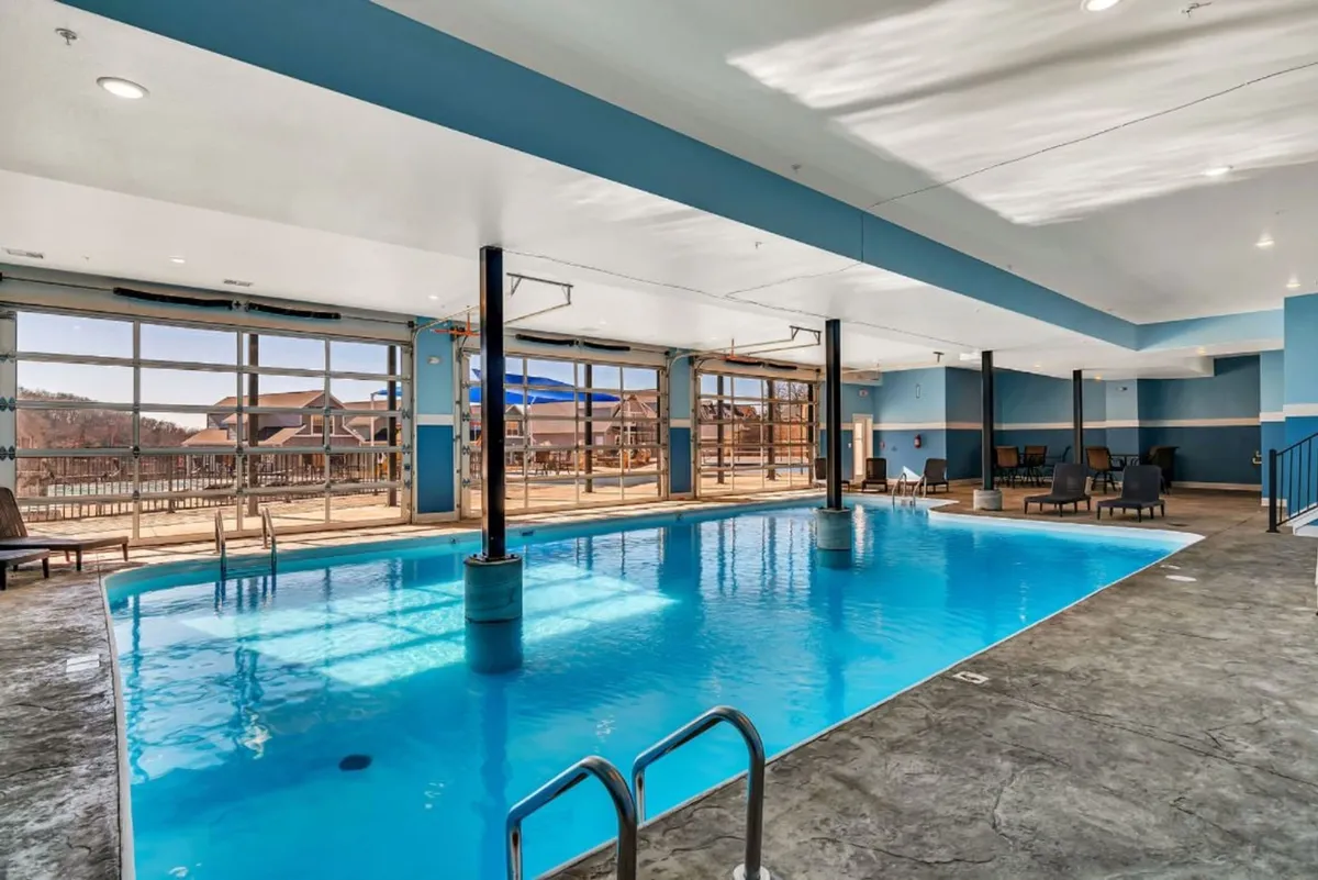 A tranquil indoor swimming pool with large windows letting in natural light, surrounded by comfortable lounge chairs. The space has a relaxed, resort-like feel, ideal for unwinding or swimming no matter the weather.