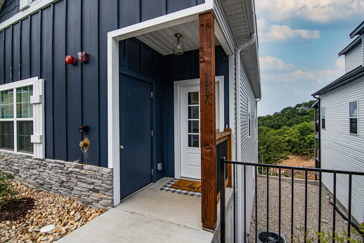 This close-up shows the front door, a welcome mat, a sturdy stone wall, and a wooden post, creating a warm, inviting first impression for arriving guests and their pets.