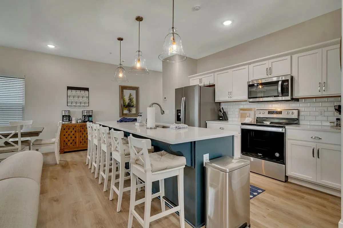 A spacious, modern kitchen with a large island, pendant lighting, stainless steel appliances, and bar stools, inviting guests to cook, dine, and entertain. The welcoming layout encourages gatherings and highlights the practical comfort of having a full kitchen for budget-friendly meal preparation.