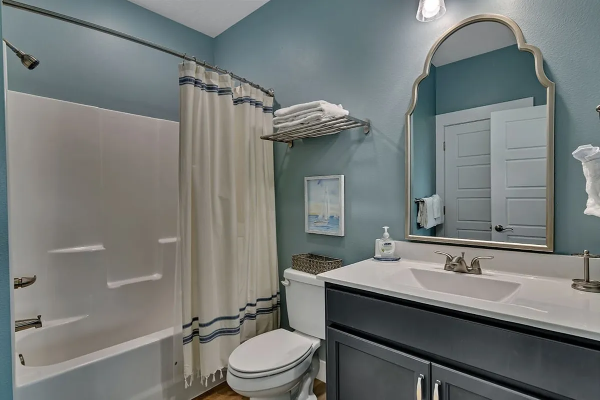 A calm, well-appointed ensuite bathroom featuring a tub, shower curtain, sink, and large mirror. The uncluttered surfaces and soothing tones create a spa-like feel, ideal for personal relaxation and rejuvenation.