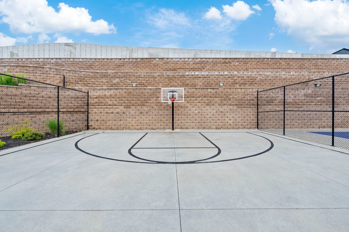 An exterior view of a basketball court featuring clear court markings, a sturdy hoop, and surrounding fencing. The space is designed for active recreation and social gatherings, inviting groups for friendly matches or energetic workouts under open skies.