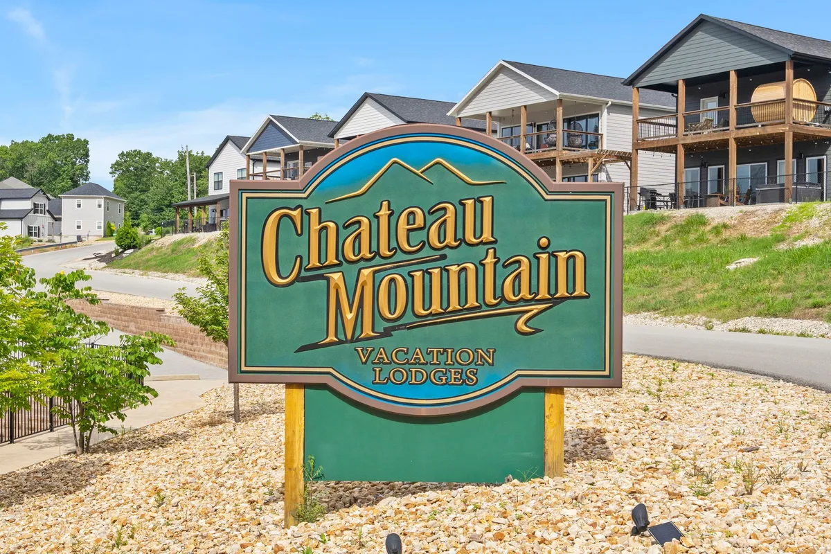 The welcoming entrance to Chateau Mountain, with a prominent sign and attractive vacation lodges set amid landscaped green spaces. The inviting setting encourages feelings of arrival and anticipation for adventure.