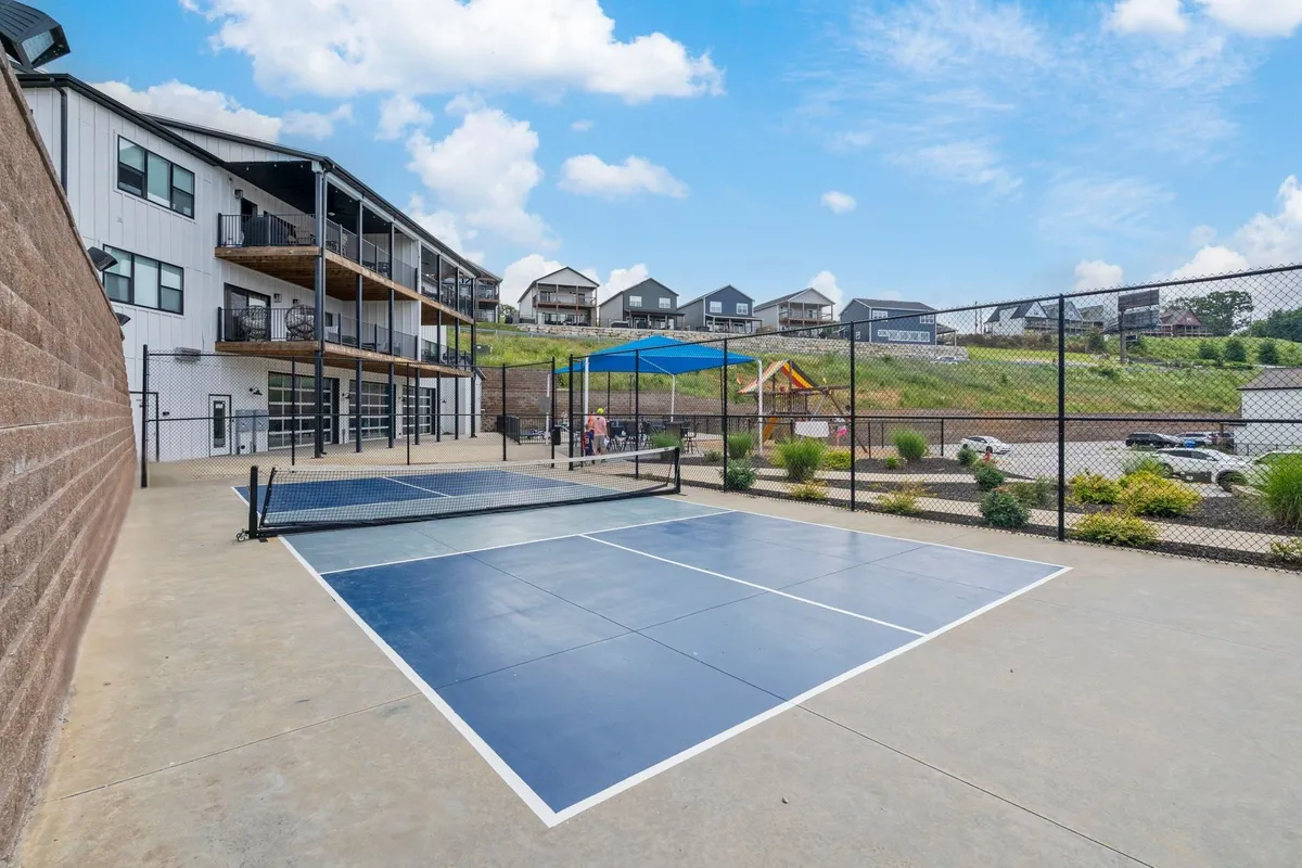 A vibrant exterior scene featuring well-kept tennis courts, a modern community building, and a playground in the background. Active guests can be seen playing tennis while others relax nearby, highlighting the range of amenities available for groups.
