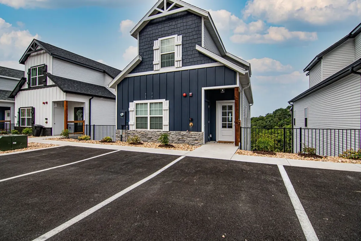 This image shows the blue and white exterior of the house with a stone foundation and a welcoming front porch, framed by a landscaped area. The open space around the home is clearly visible, offering plenty of room for outdoor activities and walks with pets.