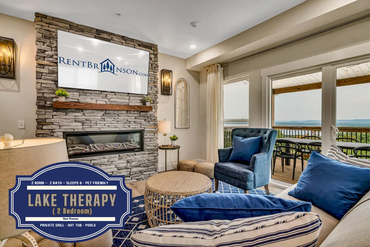 A beautifully designed living room featuring a stone fireplace, a blue armchair with decorative pillows, and expansive windows offering views of Table Rock Lake. The space is styled for comfort and relaxation, inviting guests to unwind by the fire or enjoy the scenic vista.