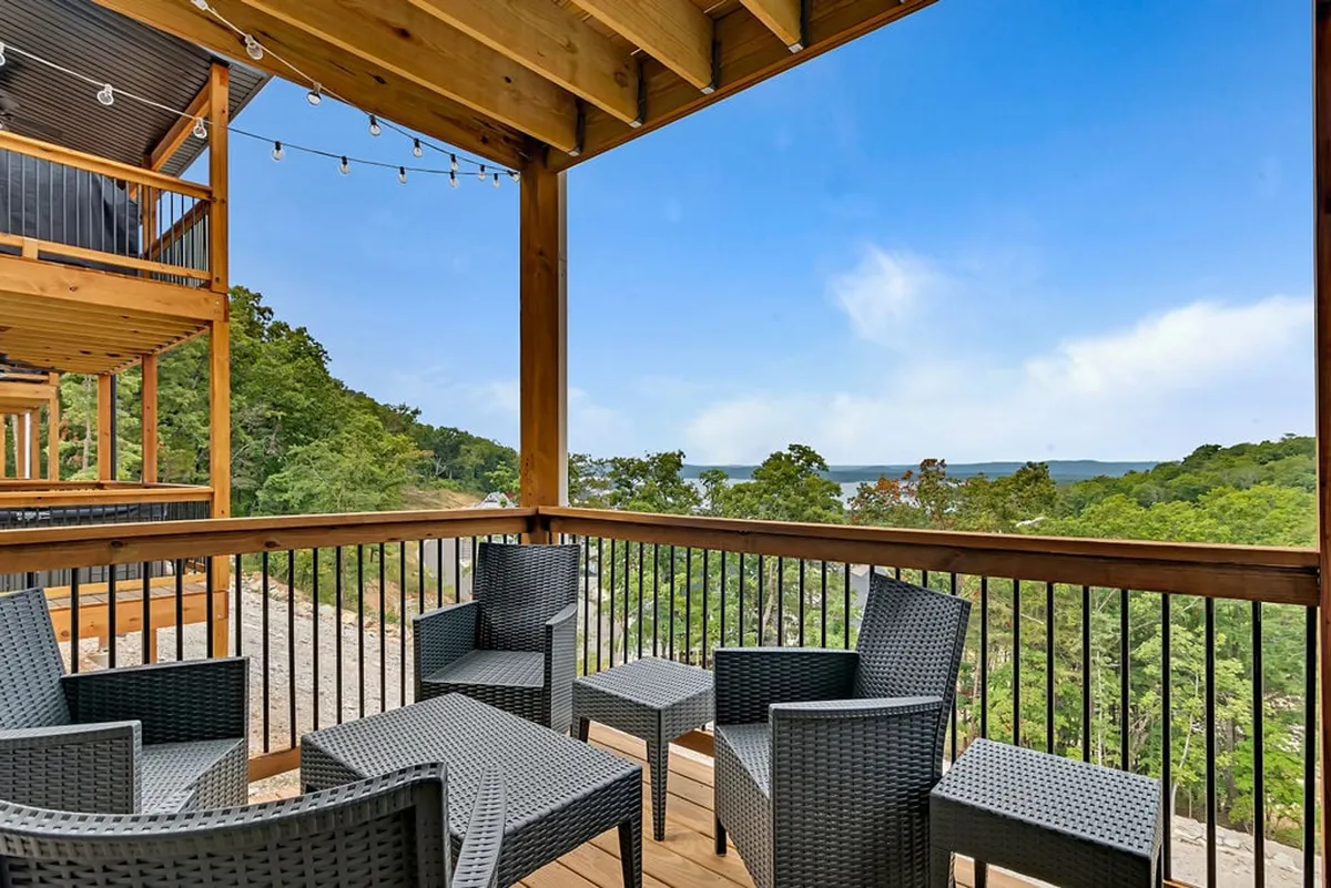 An outdoor seating area on a deck or balcony, with comfortable furniture perfect for relaxing or sharing a drink. String lights overhead add to the tranquil mood, and the view encompasses a sweeping landscape, reinforcing the sense of peaceful retreat and connection with nature.
