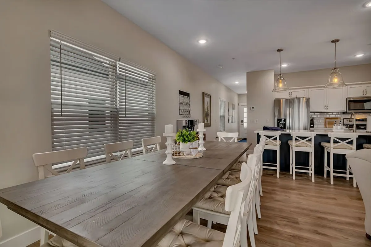 A spacious dining area with a large wooden table surrounded by white chairs, adjacent to a modern kitchen with sleek appliances. Decorative candles add a warm touch, and the open layout encourages family dinners and social gatherings.